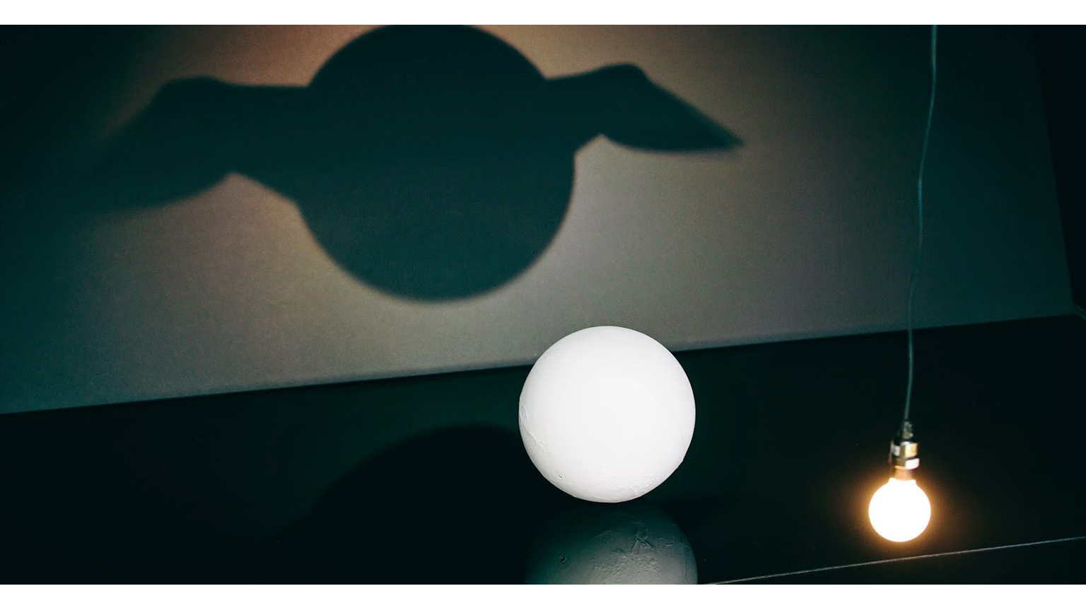 A light casting a shadow of a sphere but the shadow has wings 